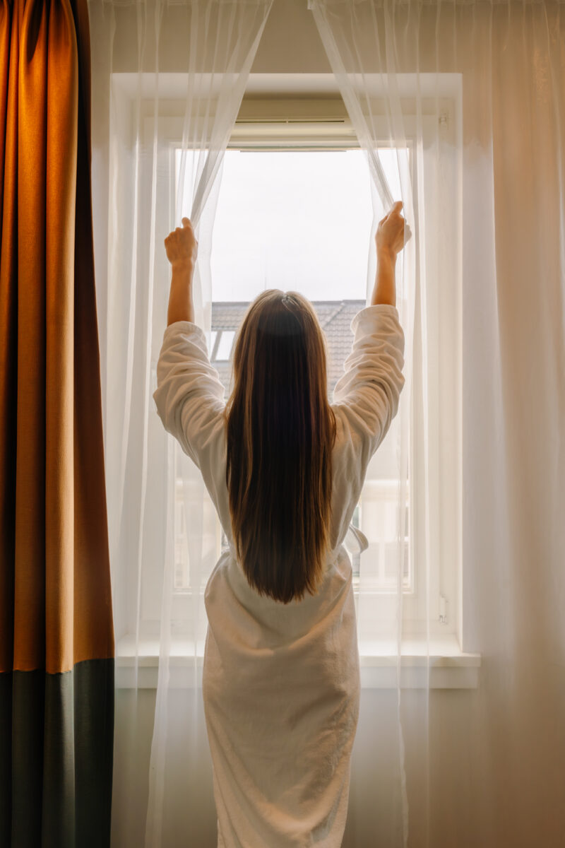 Frau öffnet Vorhang im Hotelzimmer